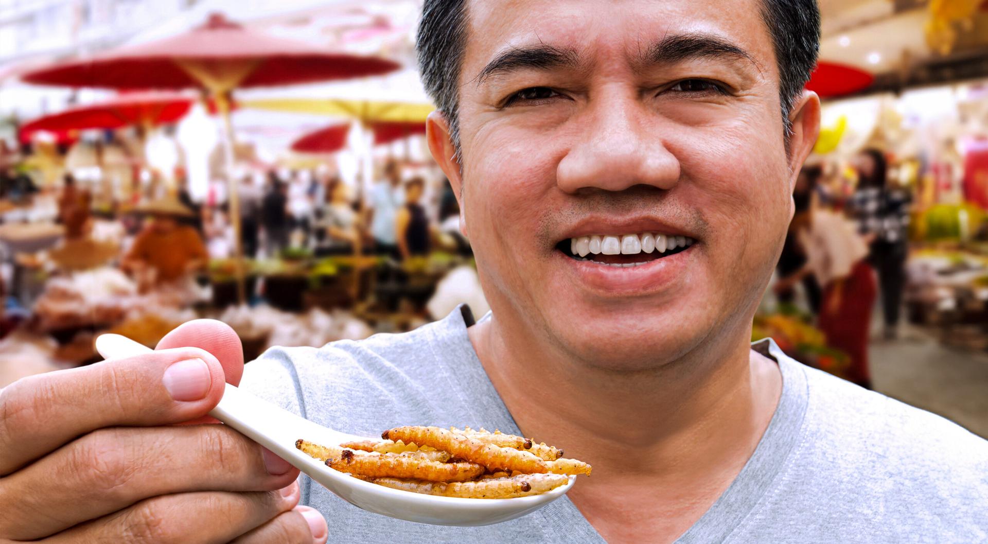A man is smiling and holding a spoon full of bugs.