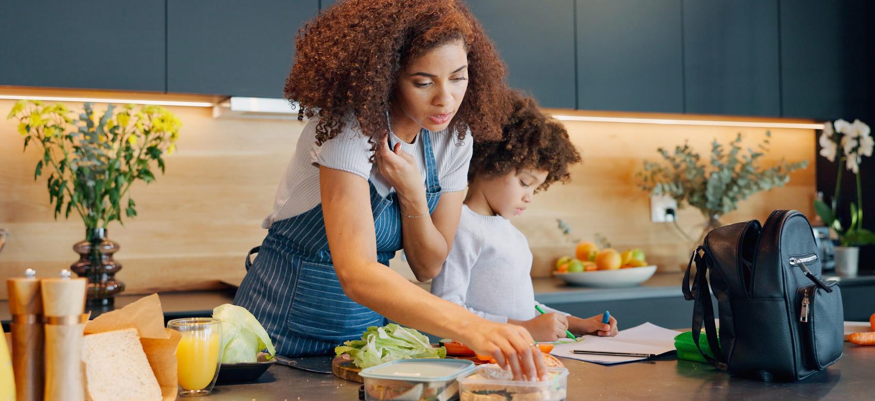 Mom in the kitchen with child, packing lunch while she is on the phone