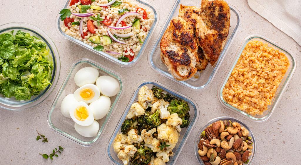 Healthy high protein meal prep with cooked chicken breast, boiled eggs, roasted vegetables, cooked lentils, couscous salad and mixed nuts