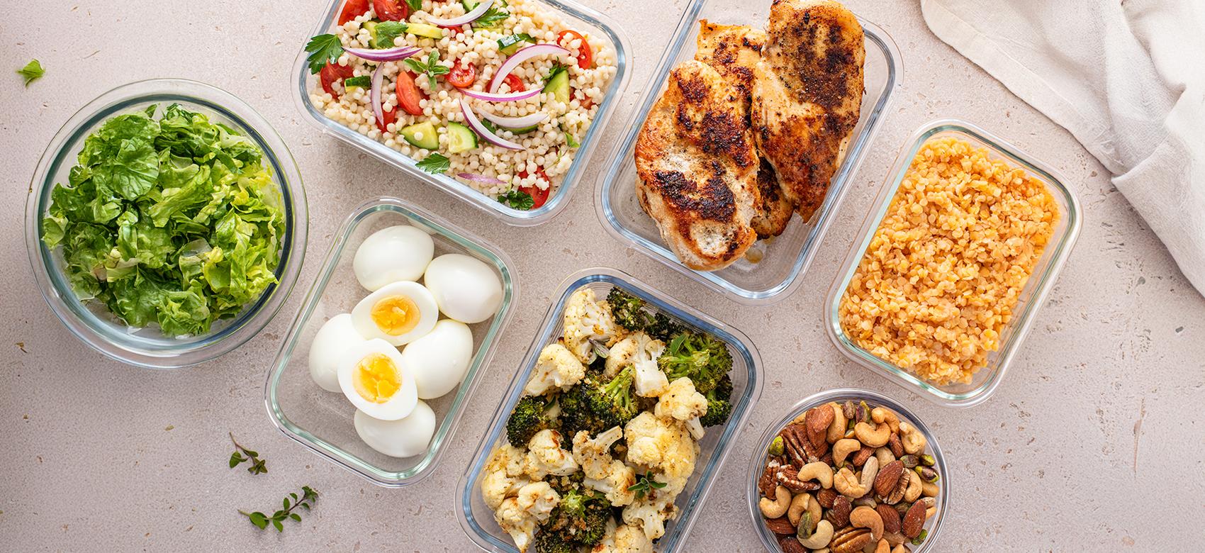 Healthy high protein meal prep with cooked chicken breast, boiled eggs, roasted vegetables, cooked lentils, couscous salad and mixed nuts