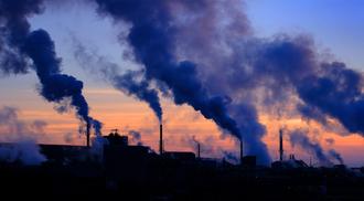 A photo of steam rising from smokestacks in a rural sunset sky.