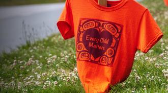 Orange shirts with the phrase "Every Child Matters" printed on them line Marine Drive in Vancouver as a memorial for the Indigenous children who were sent to Residential Schools in Canada.