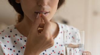 Close up cropped shot of young woman holding a glass of water prepare to swallow an orange pill.