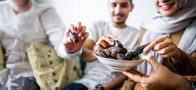 Three people, one wearing a headscarf, take dates from a bowl to break the Ramadan fast.