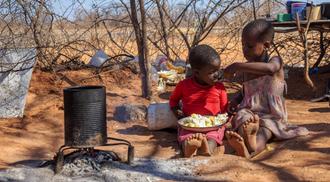 Two African children in a village near Kalahari desert, the sister feeding her brother in the outdoor kitchen