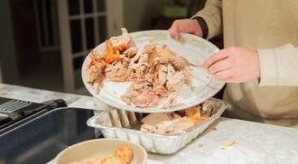 A woman is pouring leftover food from a plate into a tin tray.