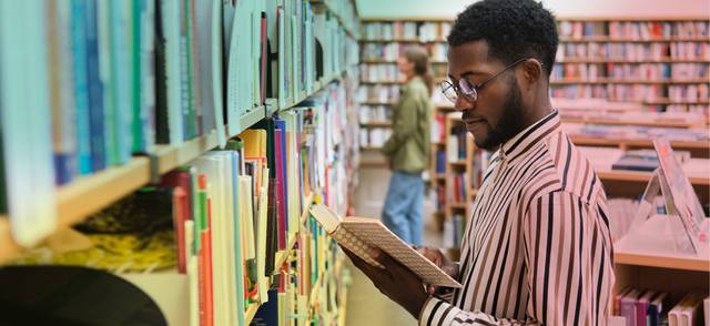 Young man in striped shirt in bookstore holding book and reading