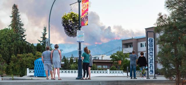 Pedestrians watch from Lakeshore Drive as a forest fire flares up in the hills above the city Penticton.