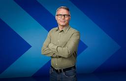 Dr. John Pawlovich, a family doctor who is the Rural Doctors’ UBC Chair on Rural Health, stands in front of a stylized chevron background