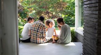A black family with a mother, father and three daughters sit beside one another on the porch.