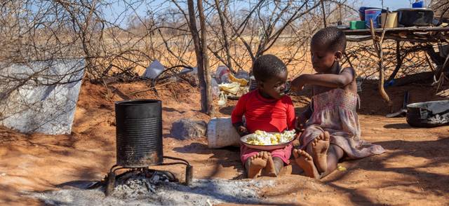 Two African children in a village near Kalahari desert, the sister feeding her brother in the outdoor kitchen