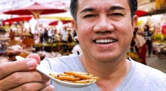 A man is smiling and holding a spoon full of bugs.