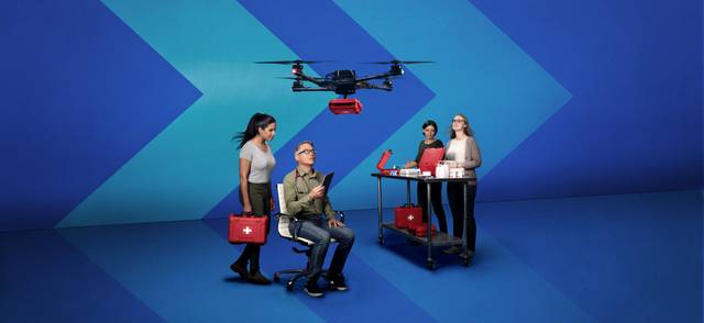 Dr. John Pawlovich, a family doctor who is the Rural Doctors’ UBC Chair on Rural Health, controls a drone overhead that carries a red box of medical supplies. Dr. Samya Vellani, students Jenna Burke and Heidi Barkman look on, equipped with other red boxes of medical supplies.