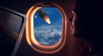 A photo of a man sitting in an airplane seat looking out the window with rocket debris flying past