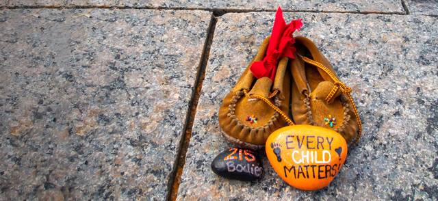 Children's shoes and a painted orange rock that reads &quot;Every Child Matters&quot; site at a memorial at Canada's Parliament Hill for Indigenous children who were sent to residential schools
