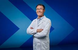 Dr. Jian Liu, an associate professor with UBC Okanagan’s School of Engineering, wears a lab coat and stands in front of a stylized chevron background.