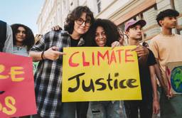 Young people participating in a climate protest. Focus is on two people embracing and holding a sign that says Climate Justice.