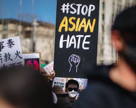 A person holds up a large #StopAsianHate sign at a large rally