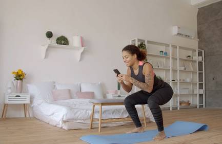 Woman doing leg squats in living room while looking at their phone