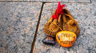Children's shoes and a painted orange rock that reads "Every Child Matters" site at a memorial at Canada's Parliament Hill for Indigenous children who were sent to Residential Schools