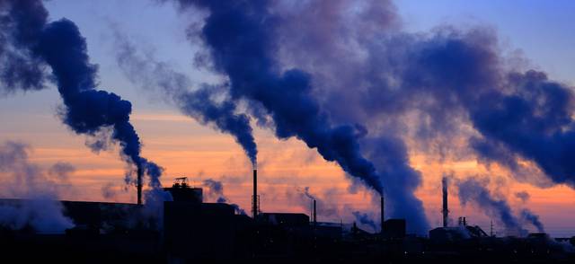 A photo of steam rising from smokestacks in a rural sunset sky.
